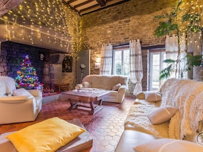 A cozy living room with a stone fireplace, a Christmas tree, and comfortable seating. - Spacious Family Home with Garden, Baby Equipment, and Game Room - Sleeps 12 (Bourguenolles)