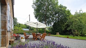 Une terrasse avec une table et des chaises, entourée de plantes de lavande et d’un mur en pierre.