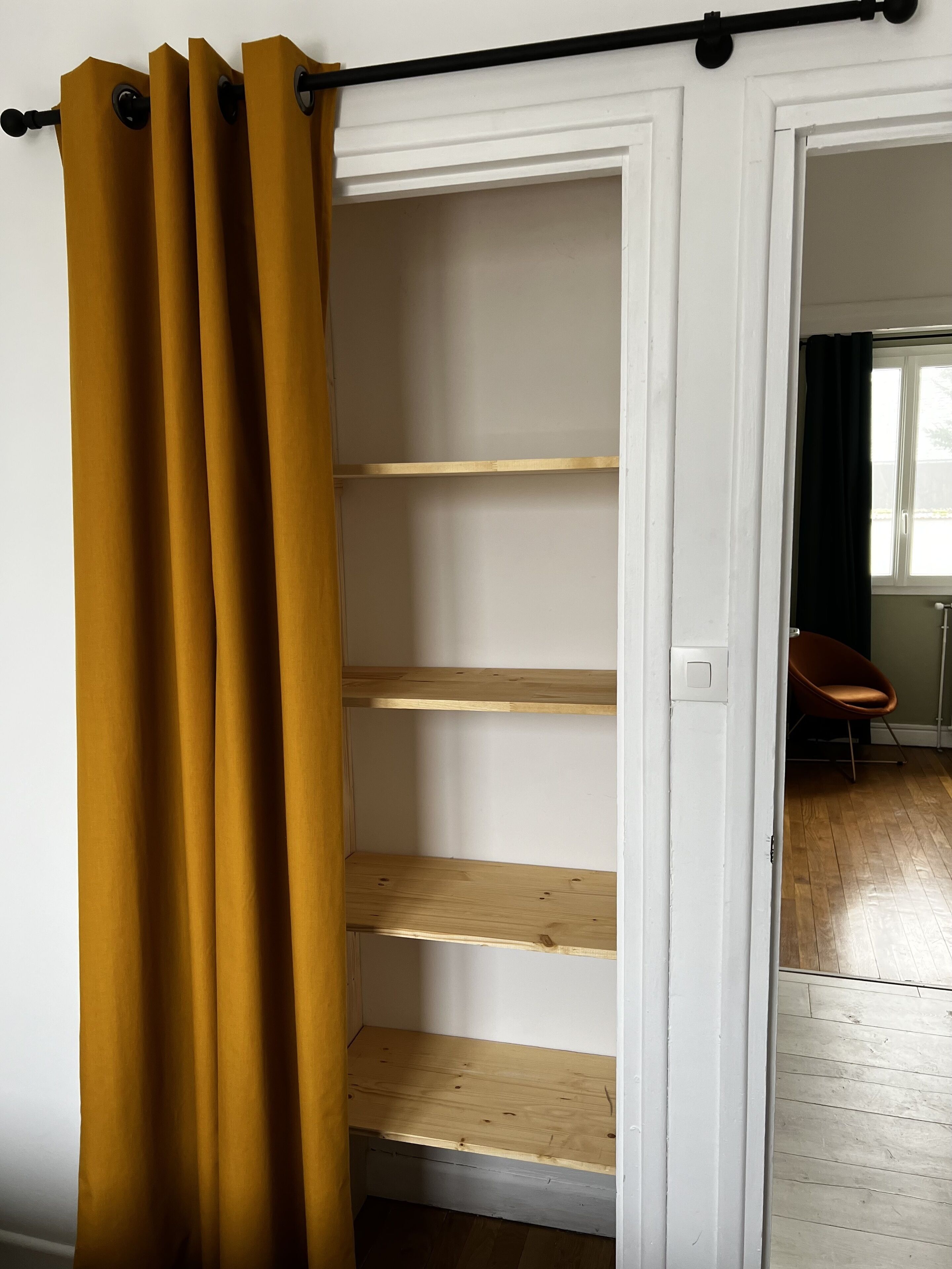 Une pièce avec une porte blanche, une étagère en bois et un rideau jaune.