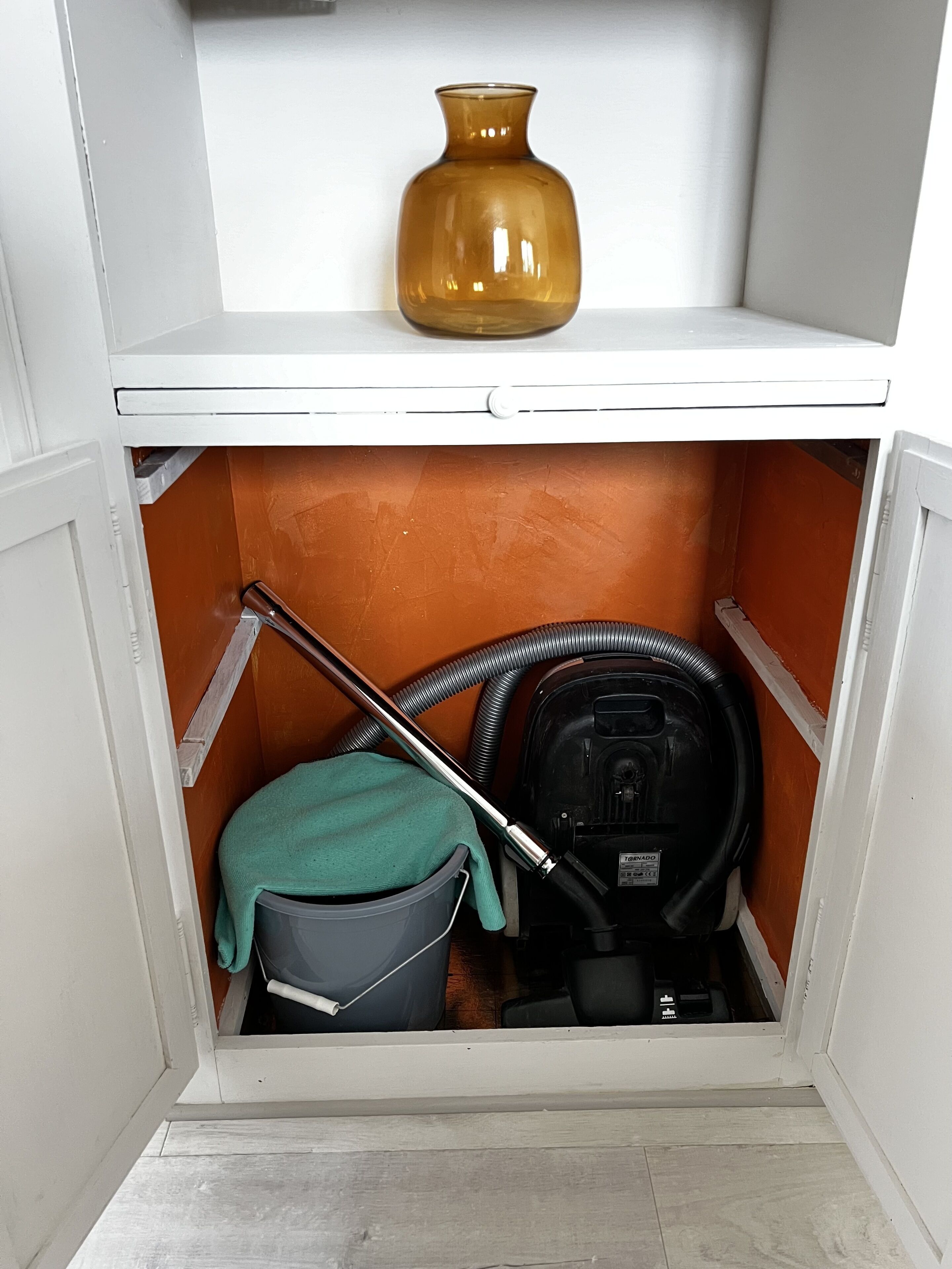 Un espacio de almacenamiento pequeño con una aspiradora, un trapeador y un cubo.