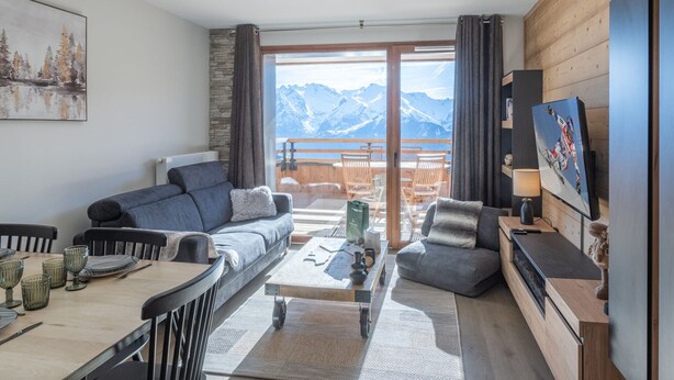 A modern living room with a sofa, coffee table, and TV, overlooking a mountain view. - Bright apartment with terrace and parking in Alpe d'Huez (Huez)