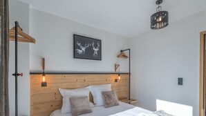 A modern bedroom with a wooden headboard, a framed deer picture, a hanging light fixture, and a bedside table with a remote control. - Bright apartment with terrace and parking in Alpe d'Huez (Huez)