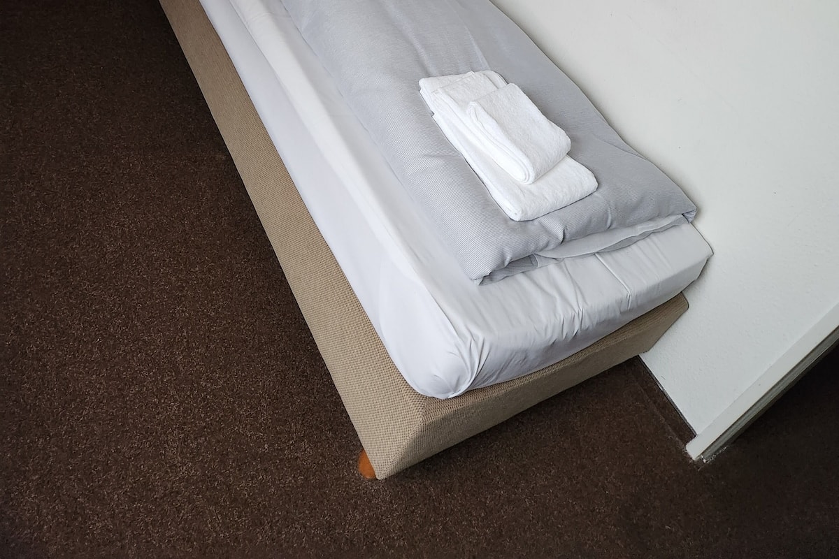 A single bed with a wooden headboard, a small wooden nightstand, and a blue wall-mounted lamp.