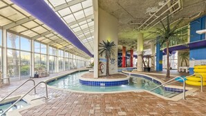 An indoor swimming pool with a brick floor, glass walls, and a ceiling with a grid pattern. - Oceanview at Dunes Village | 4 Beds & Waterpark (Myrtle Beach)
