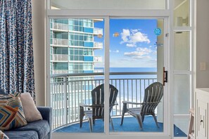 A balcony with a view of the ocean, a blue sofa with patterned cushions, and two metal chairs. - Oceanview at Dunes Village | 4 Beds & Waterpark (Myrtle Beach)