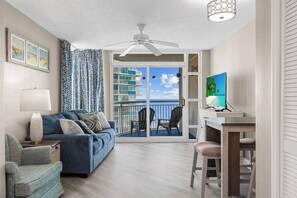 Una habitación con un sofá azul, una lámpara, un televisor y un balcón con vista al océano.