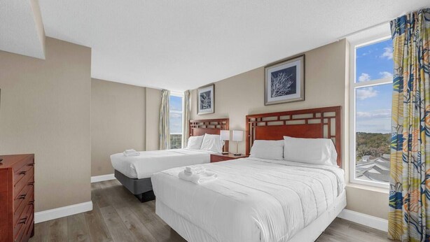 A hotel room with two beds, a wooden dresser, and a window with curtains.