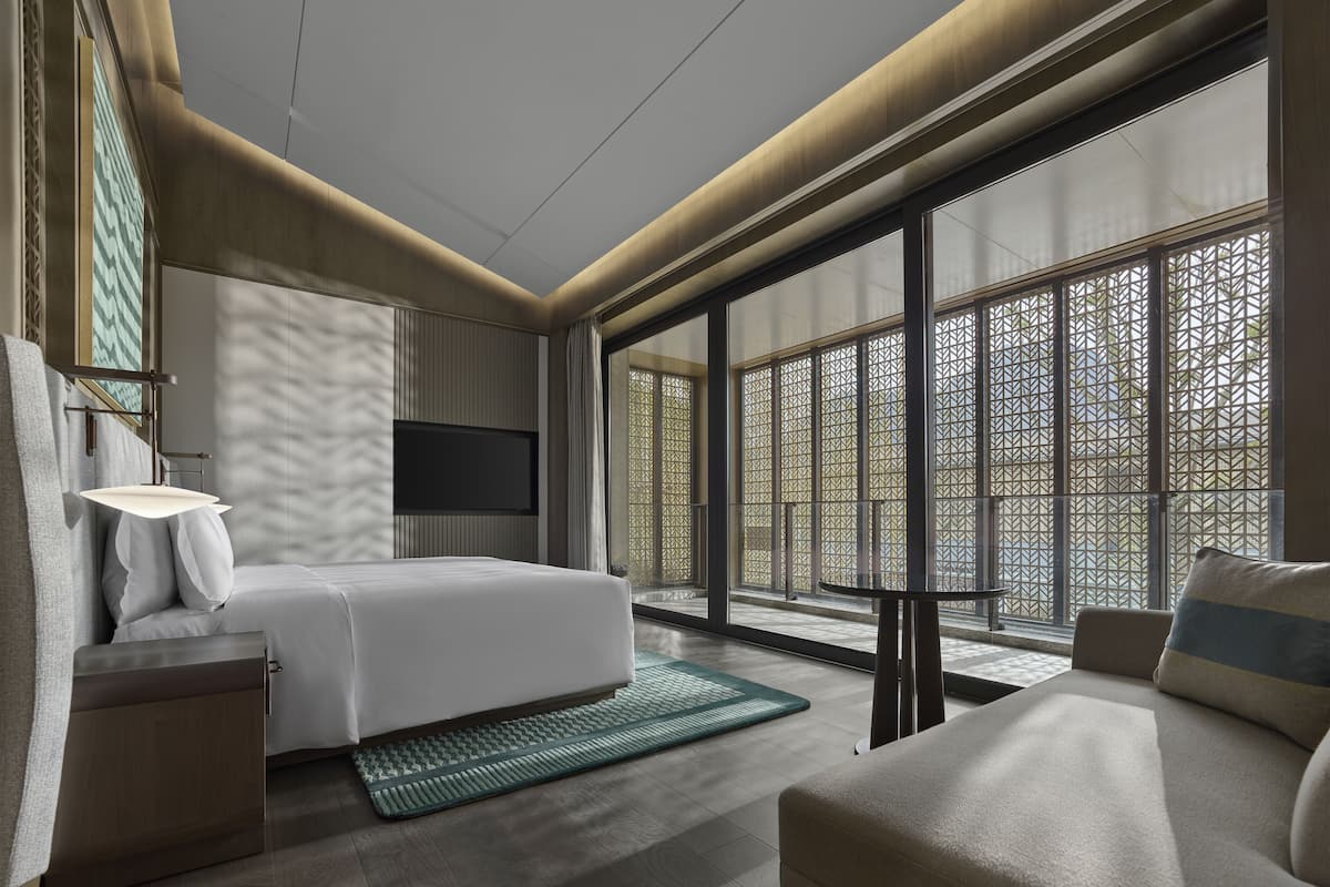 A modern hotel room with a bed, a desk, a TV, and large windows with a view.