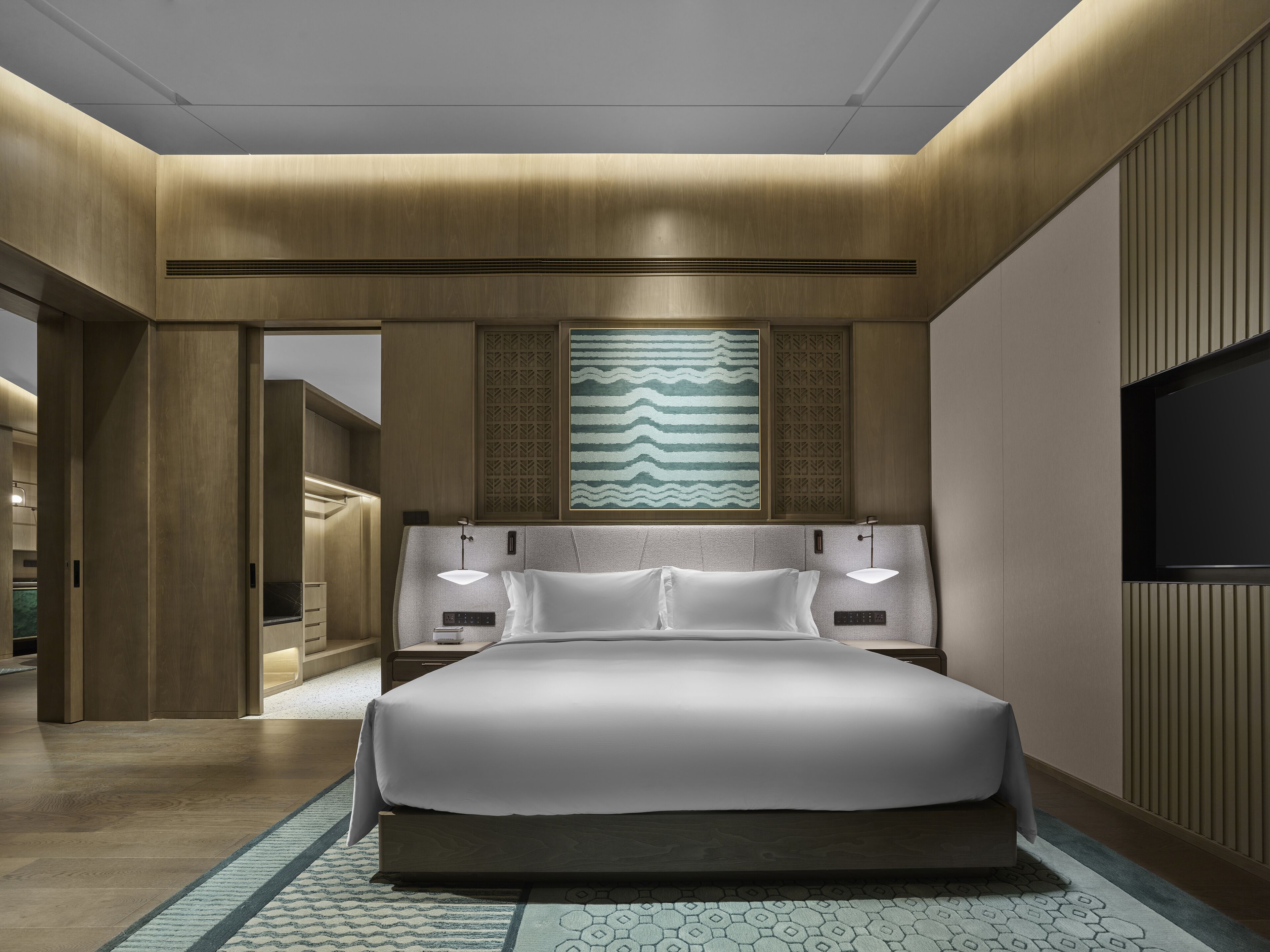A modern hotel room with a large bed, bedside tables, a TV, and a decorative wall panel.