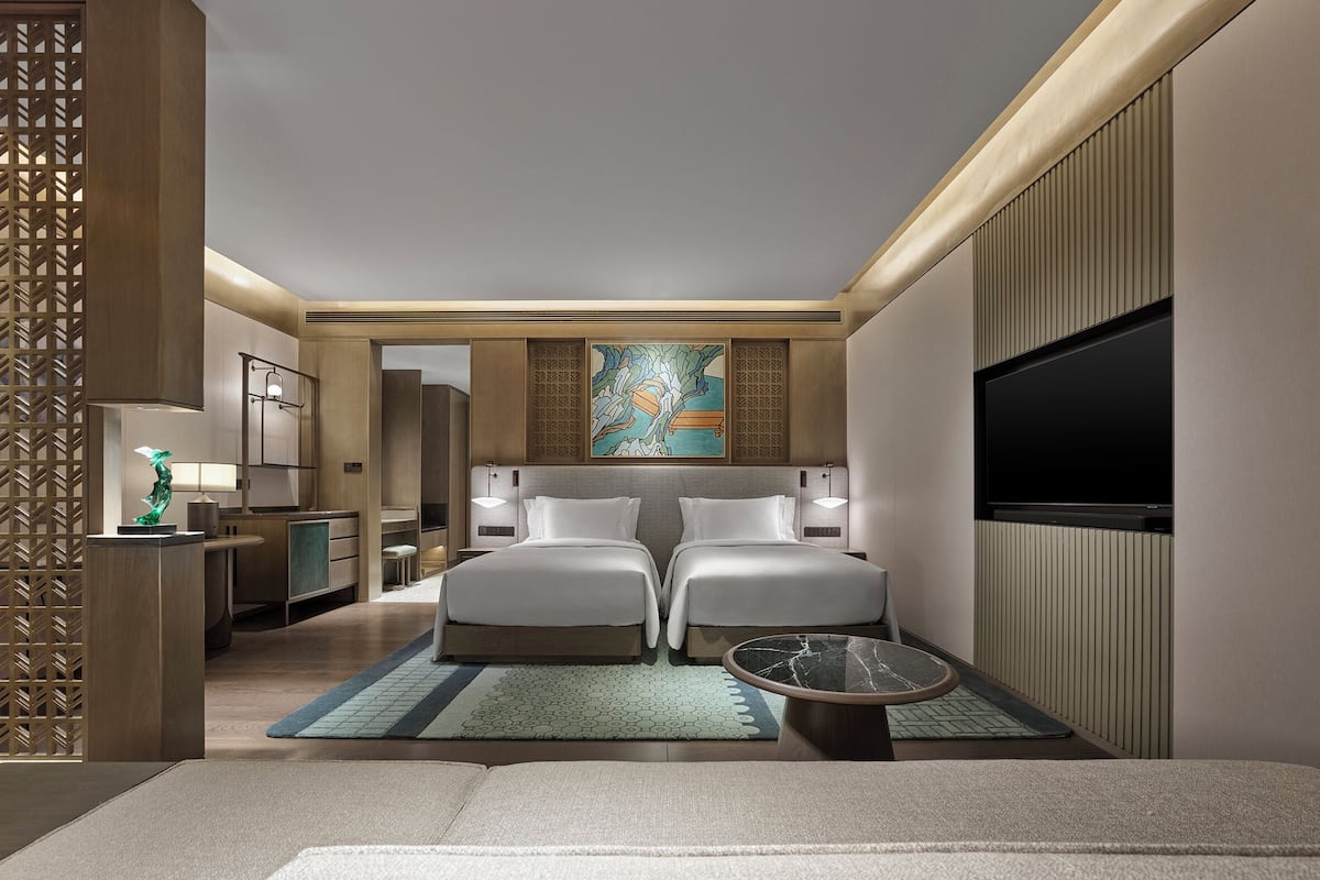 A modern hotel room with a bed, a desk, a TV, and a decorative wall piece.