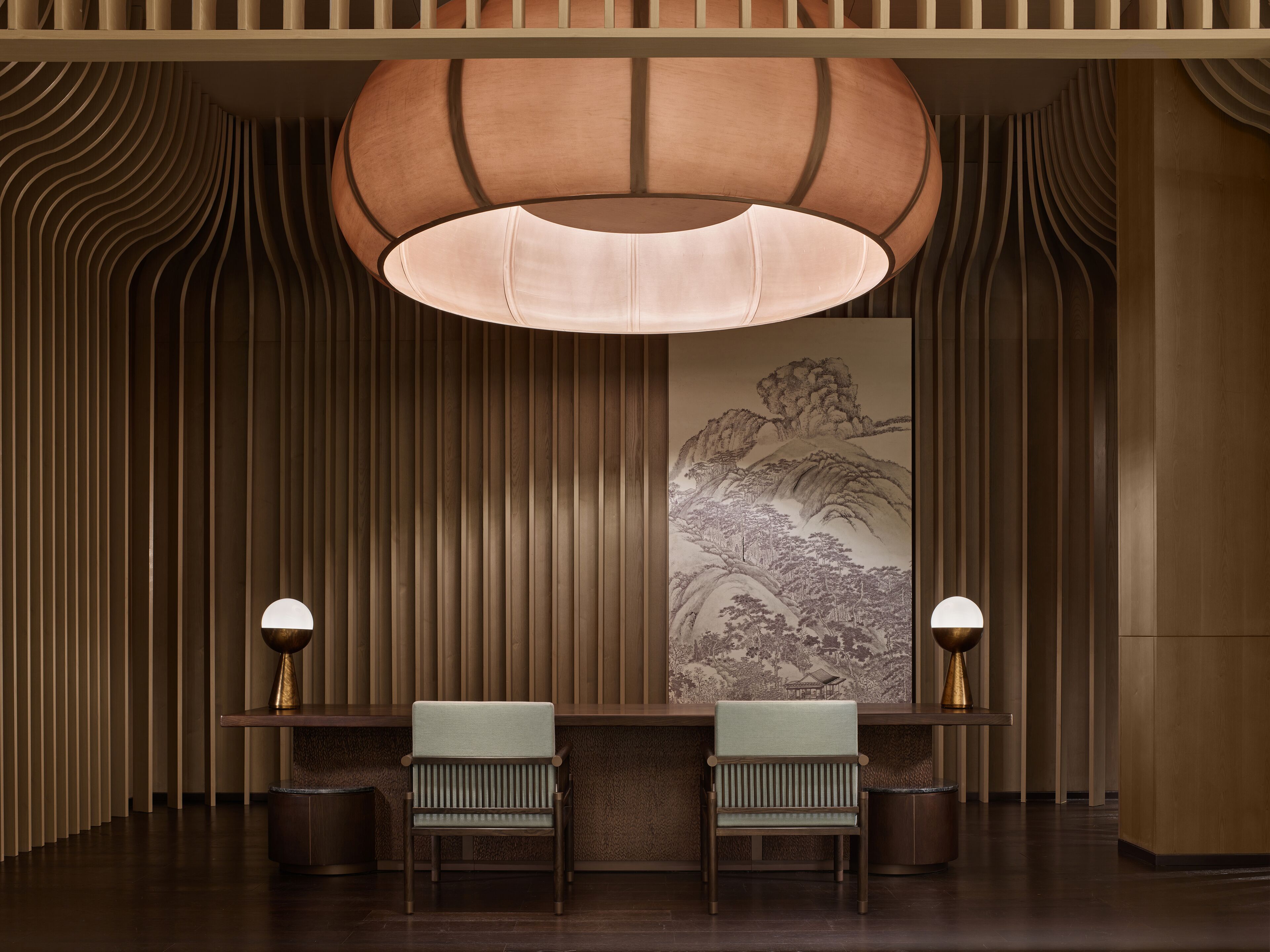 Una zona de recepción con dos sillones, una lámpara grande de pared y una obra de arte tradicional.