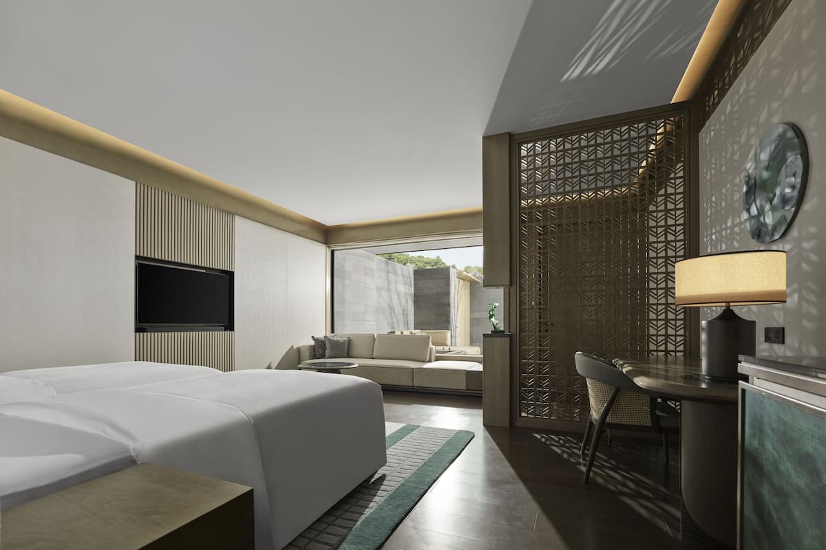 A modern hotel room with a bed, a desk, a chair, a TV, and a view of the outdoors.