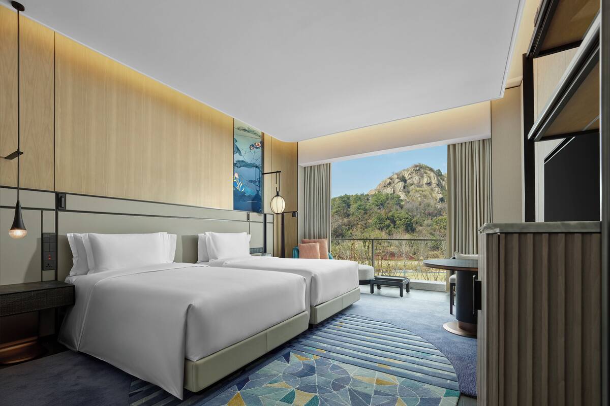 Una habitación de hotel con dos camas, un escritorio y vistas a la montaña.