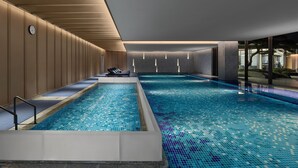 A modern indoor swimming pool with a tiled floor, a long bench area, and a clock on the wall. - Angsana Suzhou Shishan (Suzhou)