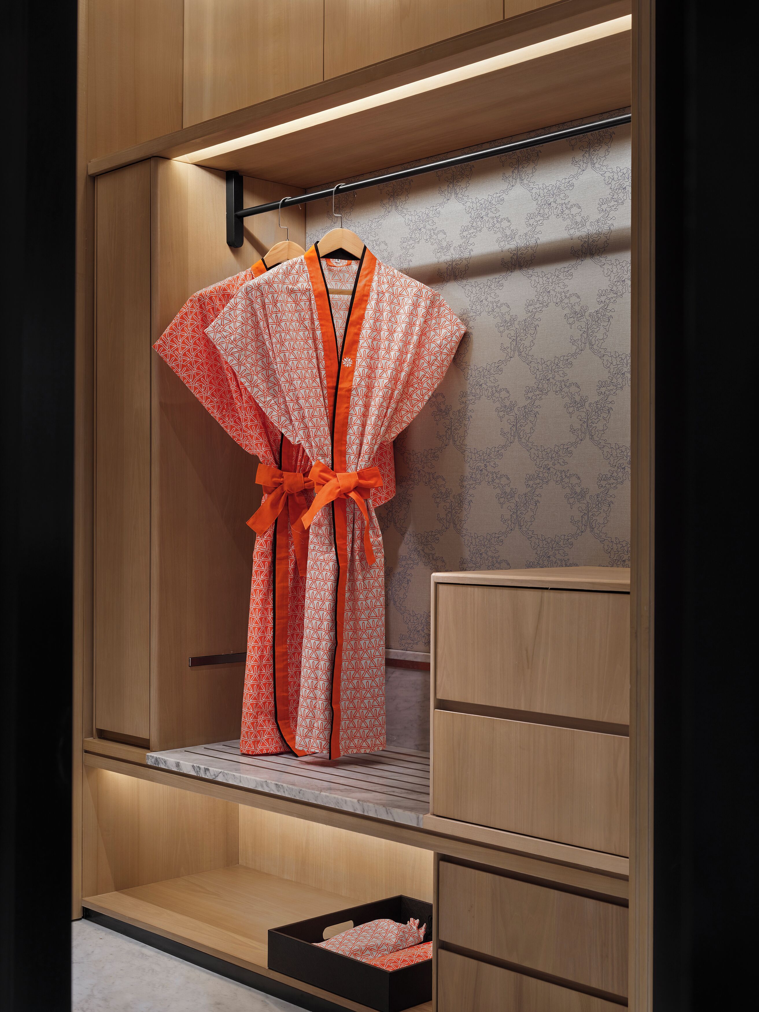 A wooden wardrobe with a robe hanging on a rod, a mirror, and a small black box on the lower shelf.