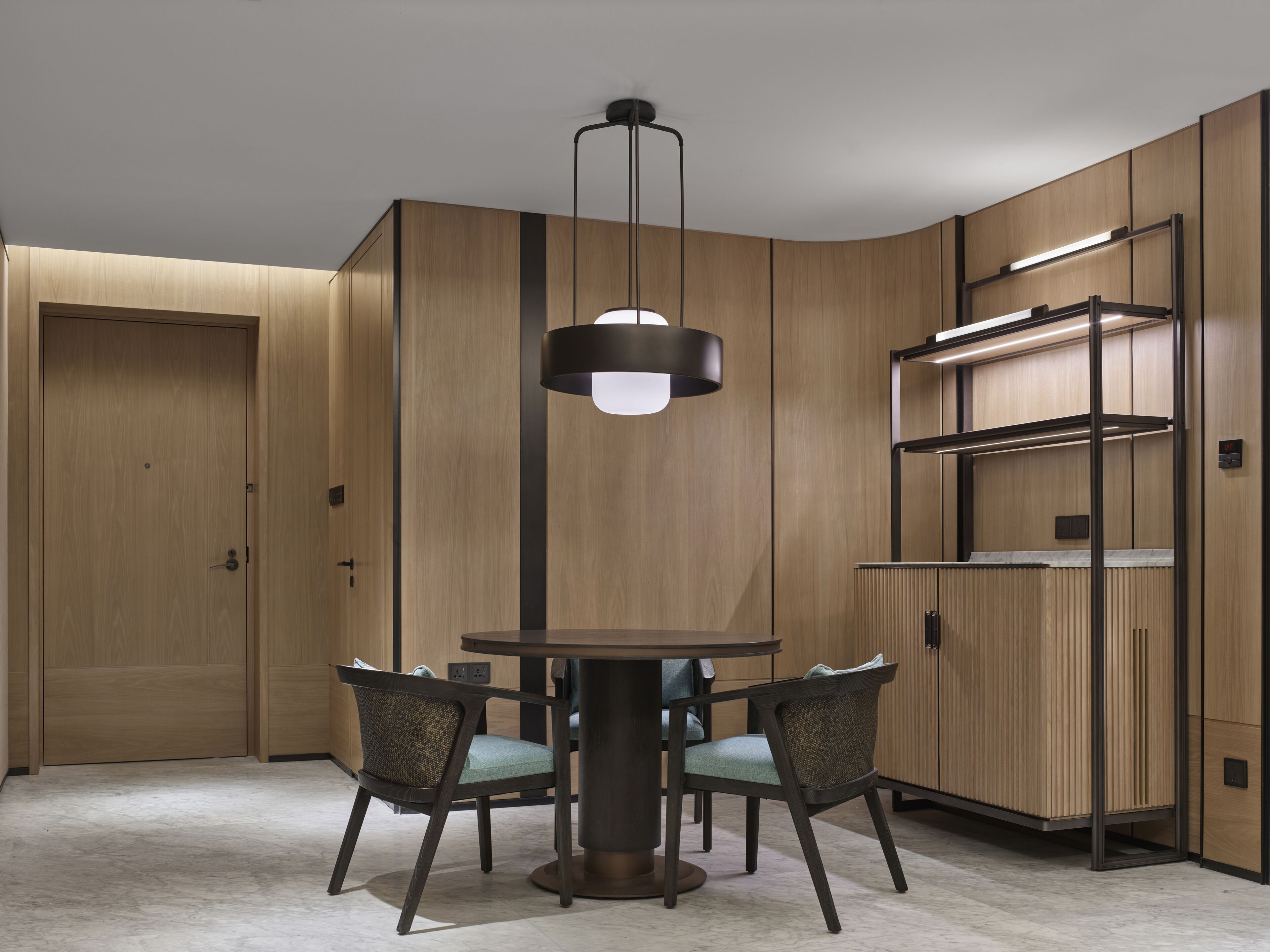 A modern dining area with a round table, four chairs, a pendant light, and built-in wooden shelving.