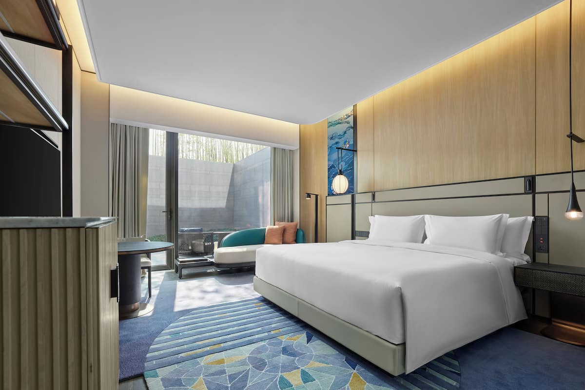 Una habitación de hotel moderna con una cama grande, un escritorio, una silla y vistas al exterior.