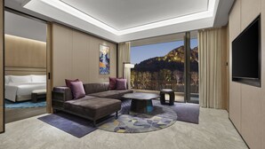 A modern hotel room with a large bed, a sofa, a coffee table, and a TV. There is a large window with a mountain view. - Angsana Suzhou Shishan (Suzhou)