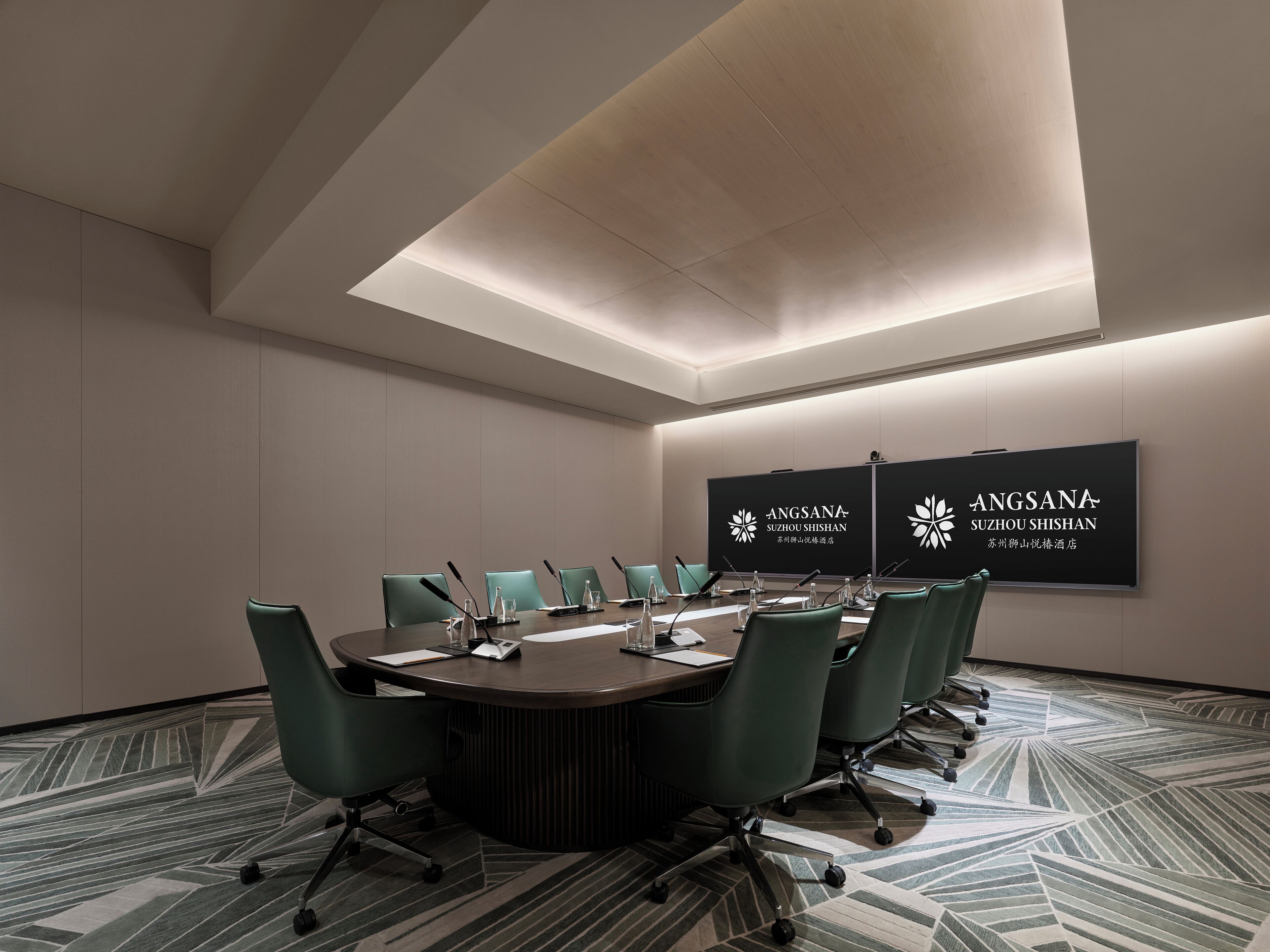Un salón de conferencias con una mesa redonda, sillas verdes y una alfombra estampada.