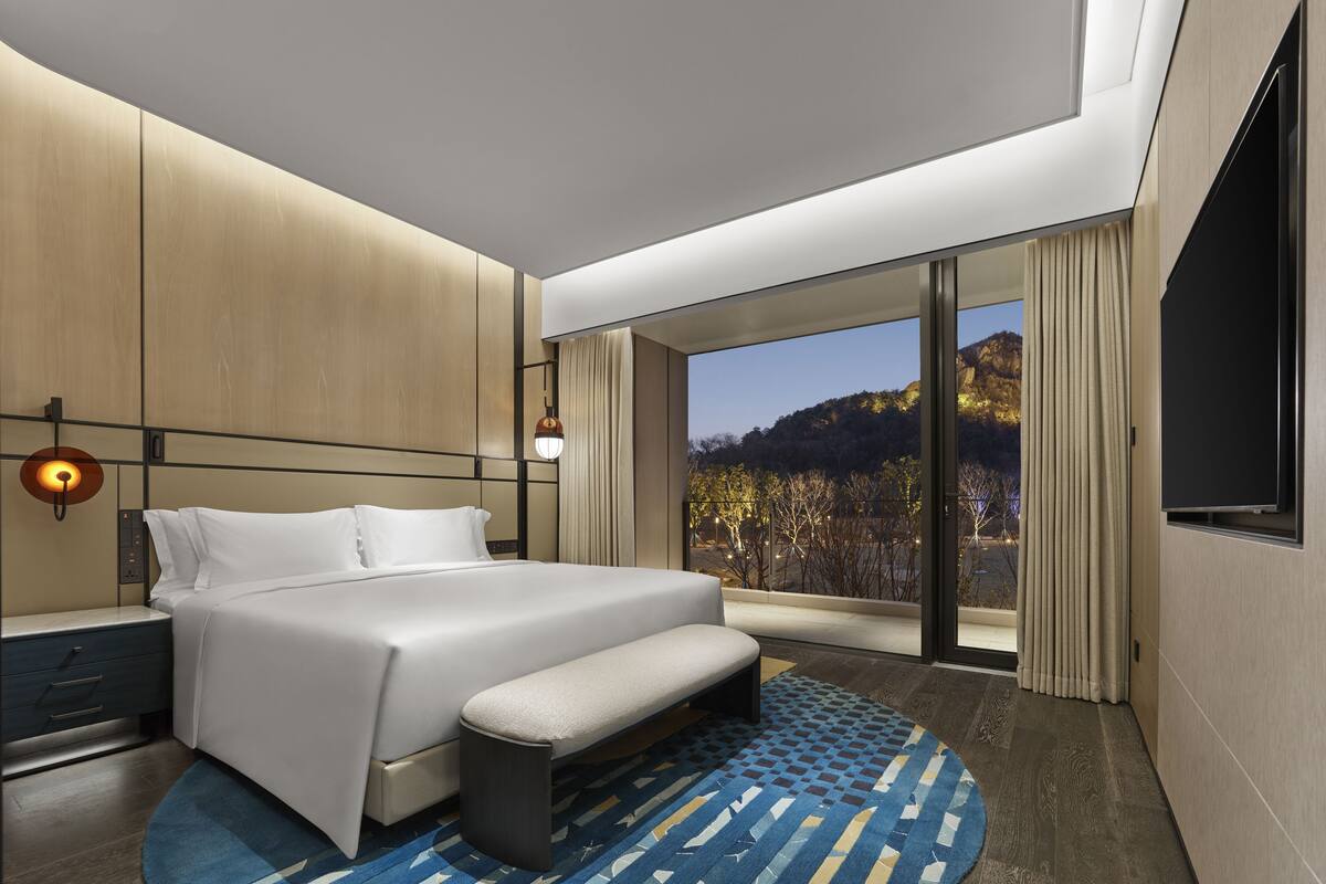Una habitación de hotel moderna con una cama grande, un banco, un escritorio y un televisor.