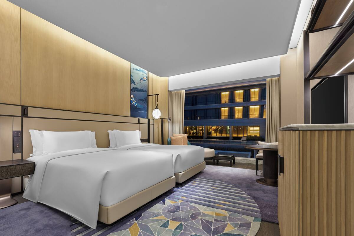 Habitación de hotel moderna con una cama grande, un escritorio y vista a la ciudad de noche.