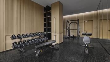 Un gimnasio moderno con pared de espejos, estantes para pesas, mancuernas, una prensa de banca y una estructura para sentadillas.