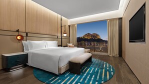 A modern hotel room with a large bed, a nightstand, a TV, and a view of a mountain. - Angsana Suzhou Shishan (Suzhou)