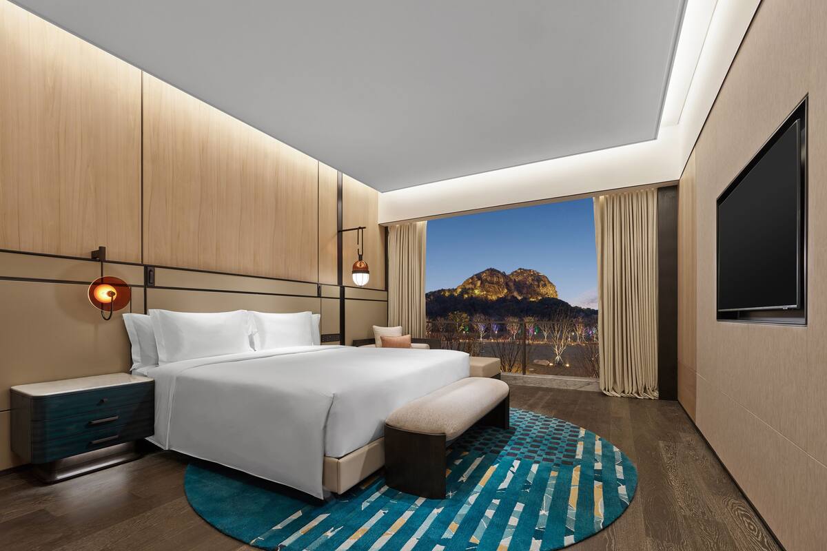 Una habitación de hotel moderna con una cama grande, una mesita de noche, un televisor y vistas a la montaña.