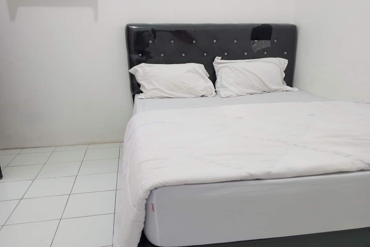 A neatly made bed with white bedding in a room with white tiled flooring and a dark headboard.