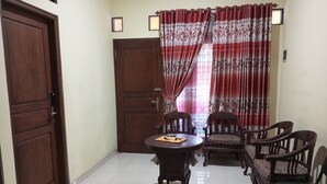 A room with a wooden door, a round table with chairs, and a window with red curtains. - OYO Life 92543 Ratu Sakti Residence Syariah (Semarang)