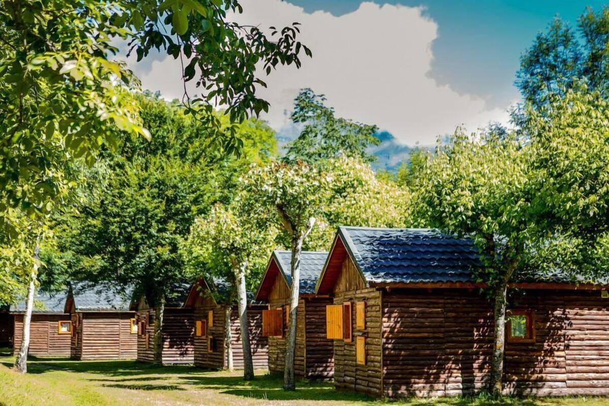 Une rangée de cabanes en rondins, avec un ciel dégagé et une végétation luxuriante en arrière-plan.