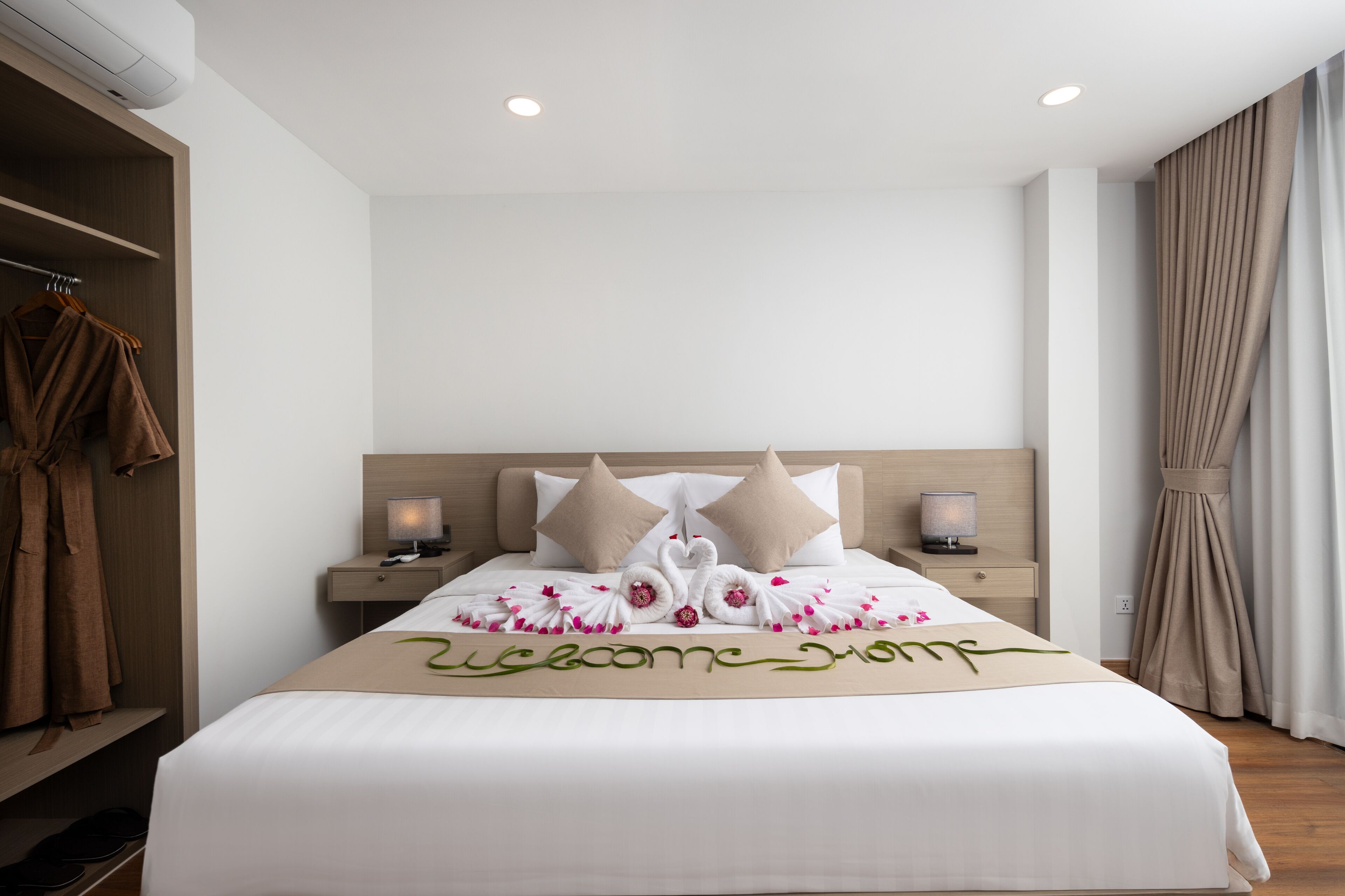 A neatly made bed with a welcome mat, two pillows, and a bedside table with a lamp.