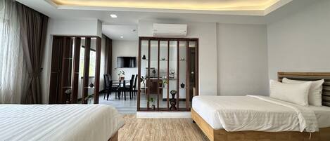 A hotel room with two beds, a dining area with a table and chairs, and a kitchen visible through a partition.