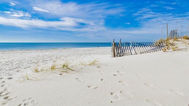 Une plage de sable avec des empreintes et une clôture en bois.