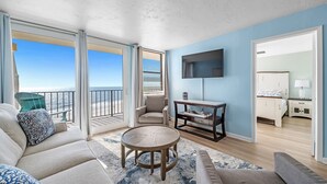 A spacious living area with a balcony overlooking the beach, a sofa, a coffee table, and a TV mounted on the wall. - Beachfront Gulf House, 602, Sea South Properties (Gulf Shores)