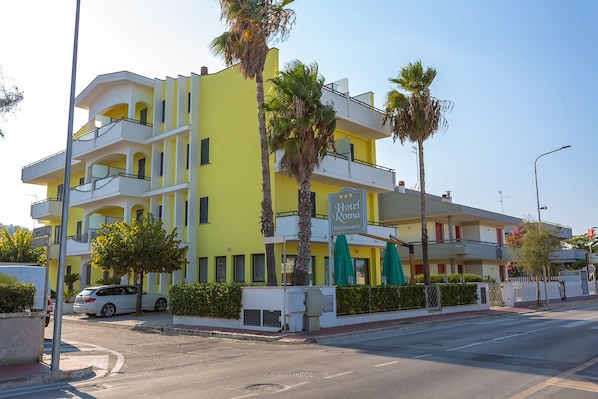 Un hotel de varios pisos con balcones, un letrero de restaurante y palmeras.