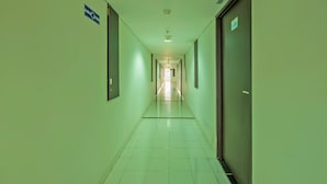 Un pasillo largo y estrecho con paredes verdes y suelo de baldosas, que conduce a una salida luminosa al final.