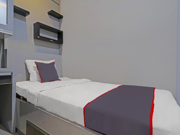 A modern hotel room with a neatly made bed, a bedside table, and a built-in shelf above the bed. - OYO Life 92649 Jarrdin Apartment By Glory (Bandung)
