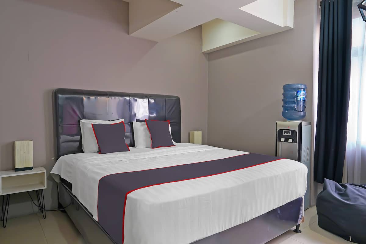 A neatly made bed with a grey headboard, a water dispenser, and a large water bottle on a stand.