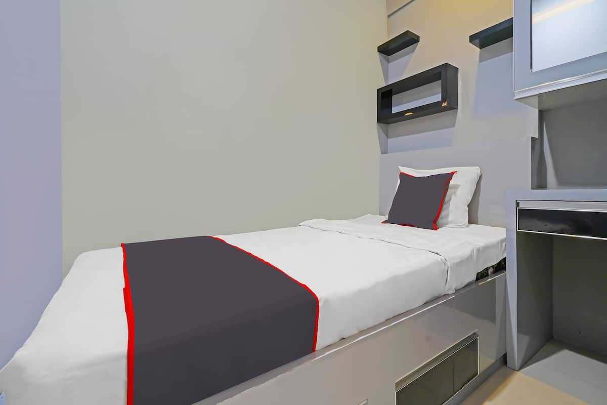 A compact bed with a white and black bedspread, a single pillow, and a bedside table with a mirror.