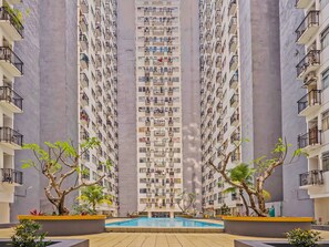 A high-rise residential building with multiple balconies, a central swimming pool, and surrounding greenery. - OYO Life 92649 Jarrdin Apartment By Glory (Bandung)