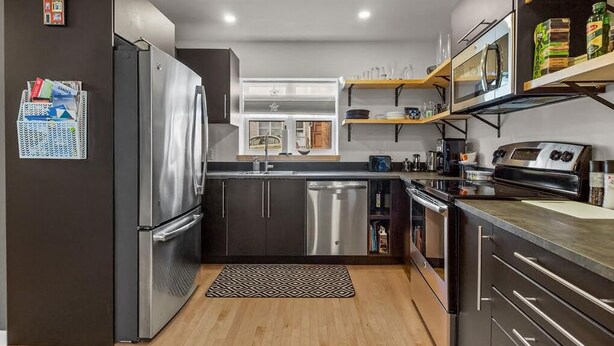 Een moderne keuken met roestvrijstalen apparatuur, houten vloeren en inbouwplanken.
