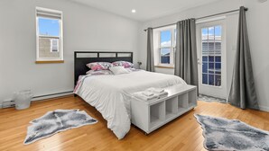 Een slaapkamer met een bed, een bankje, twee ramen en een deur.