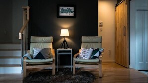 Een gezellige woonkamer met twee fauteuils, een klein bijzettafeltje met een lamp, en een donkere muur met een ingelijst kunstwerk.