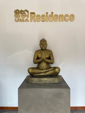 A statue of a seated figure in a meditative pose, placed on a pedestal, with a sign above reading "UMA Residence". - UMA Residence (Siem Reap)