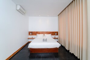 A hotel room with a wooden headboard, a large bed with white bedding, a nightstand, and a wall-mounted air conditioner. - UMA Residence (Siem Reap)