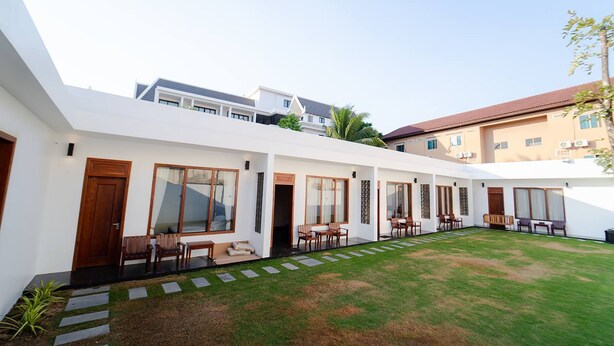 A modern building with a covered outdoor area featuring multiple seating arrangements and a well-maintained lawn. - UMA Residence (Siem Reap)