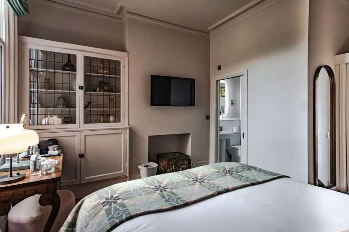 A hotel room with a bed, a desk with a lamp, a television, a wardrobe, and a mirror.