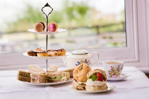A table with sandwiches, scones, macarons, and a teapot.