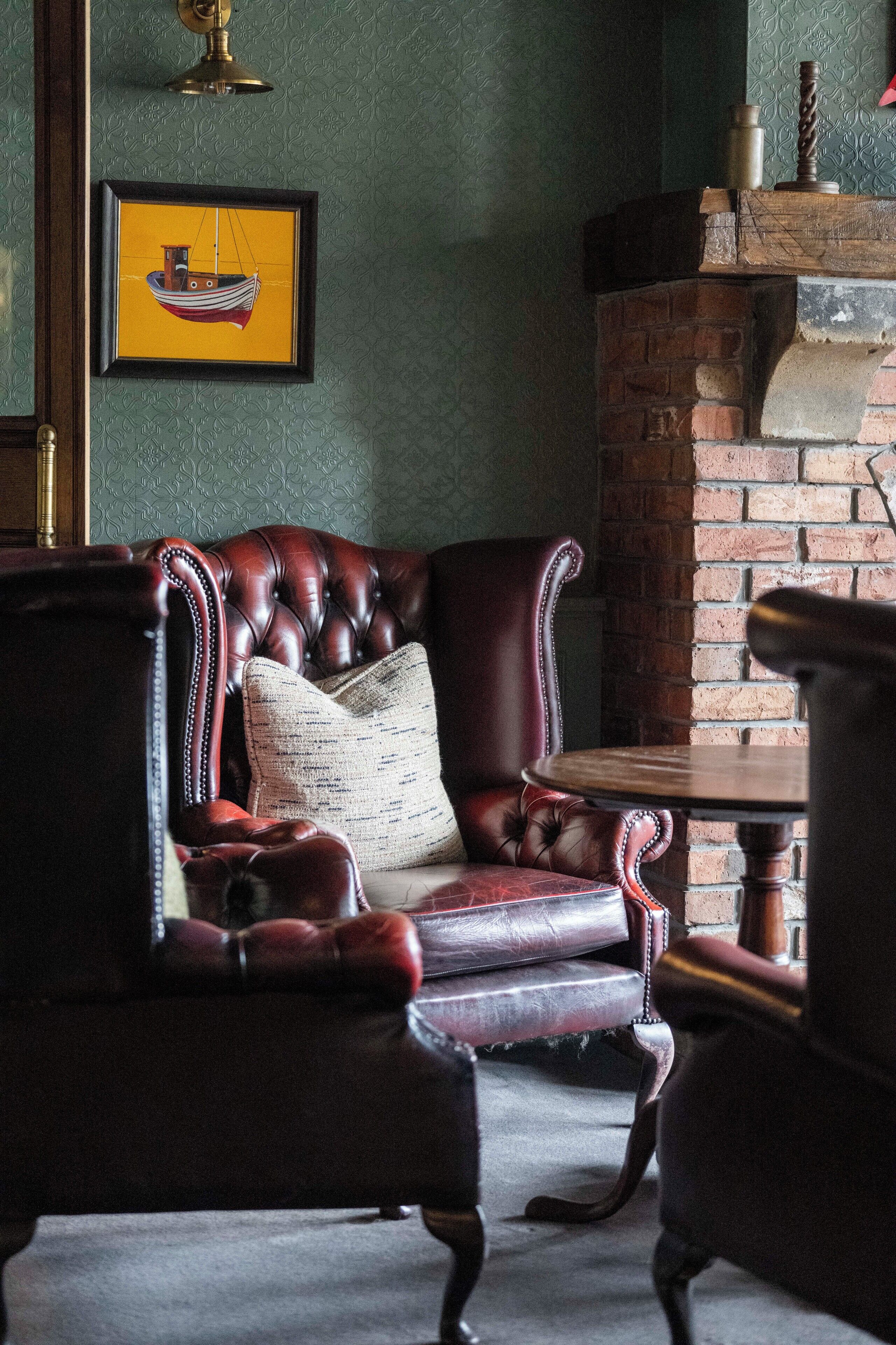 Una habitación con un sillón de cuero, una mesita y una chimenea.